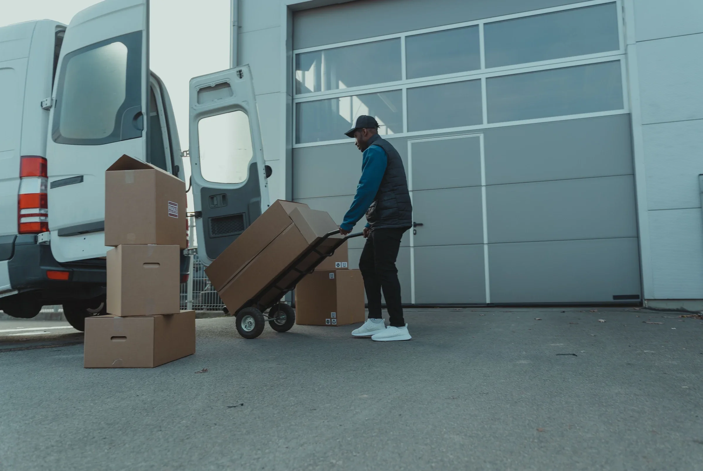 Warenübergabe mit Transporter und Sackkarre an einem Gewerbegebäude; Symbolfoto
